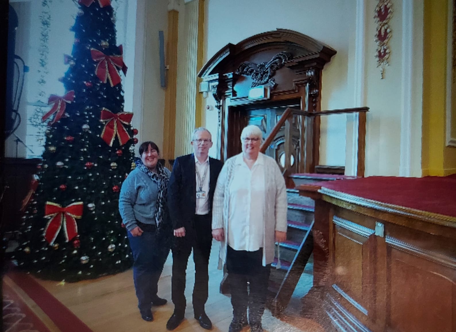 Image shows three reps standing by a Christmas tree in Belfast City Hall.