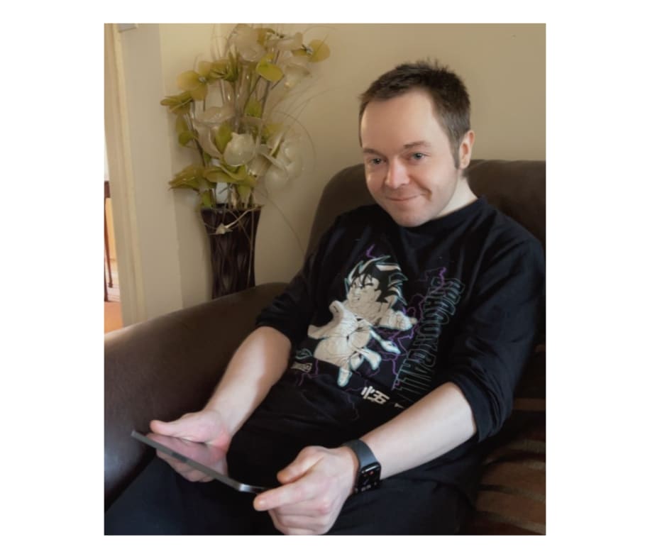 Peter sitting on sofa holding tablet and smiling at camera.