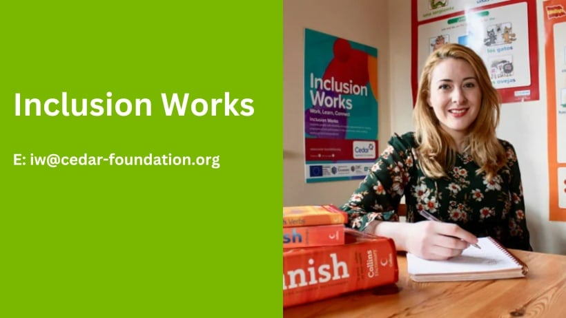 Woman with long red hair sitting at desk smiling with Spanish text books. Inclusion Works. Email iw@cedar-foundation.org